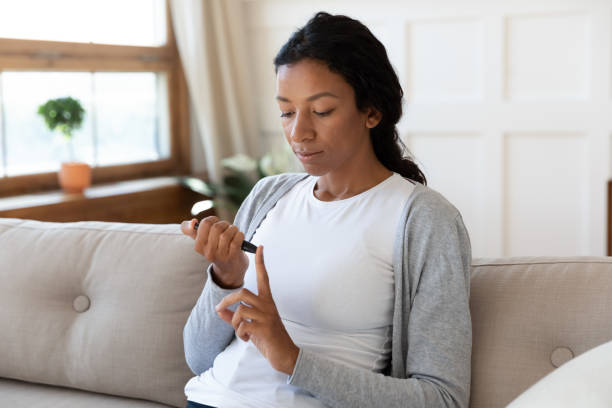 African American woman measure blood sugar level at home Young African American woman sit on couch at home do daily checkup glucose test with glucometer, biracial millennial female pinch finger measure blood sugar level at home, diabetes problem concept scalpel photos stock pictures, royalty-free photos & images