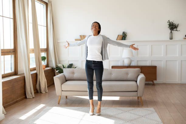 Happy african American woman dancing at home in living room Happy African American young woman stand dance in bright modern living room meet welcome new day, overjoyed smiling biracial female feel optimistic excited, celebrating good news at home resilience photos stock pictures, royalty-free photos & images