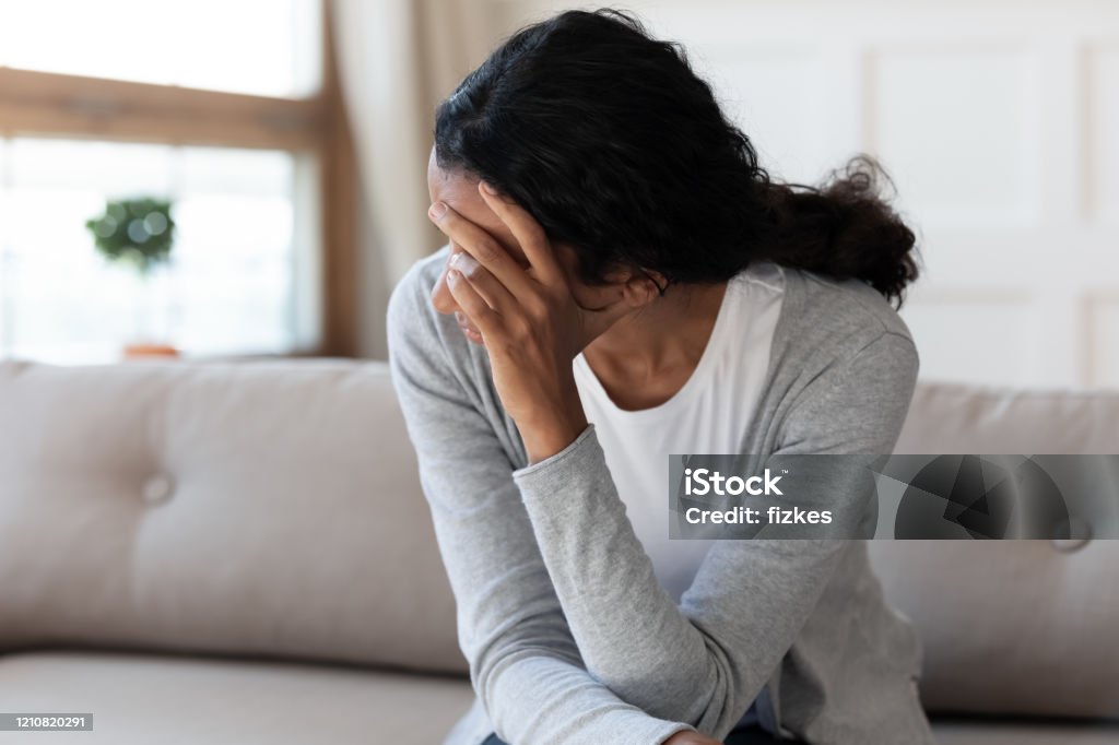 Unhappy biracial woman look in distance feeling depressed Unhappy biracial young woman sit on couch at home look in distance feel depressed sad, upset African American female lost in thoughts, suffer from miscarriage or abortion, psychological help concept Miscarriage Stock Photo