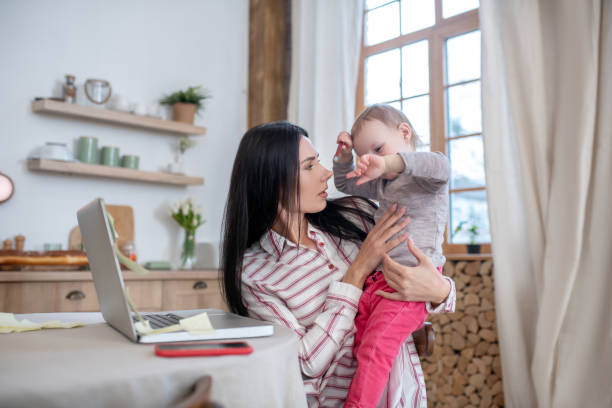 istock Young mom holding baby, distracted from work 1210824248