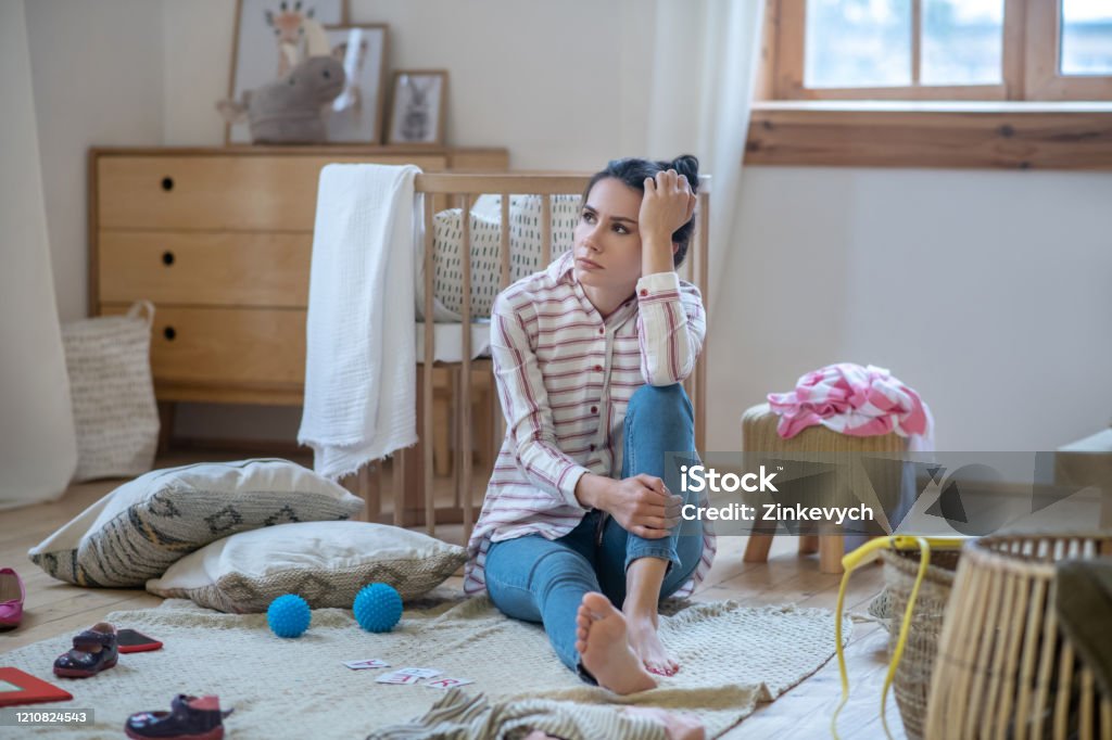 Tired woman sitting on the floor in messy room At home. Tired woman sitting on the floor in messy room, propping up her head Mother Stock Photo