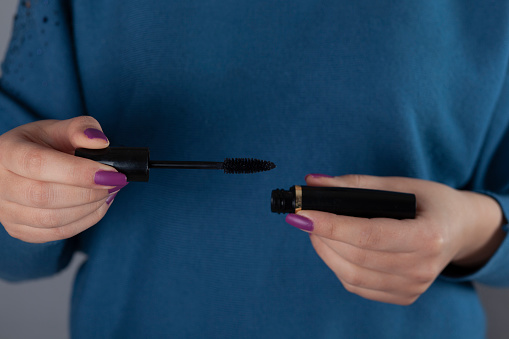 woman hand Mascara on the grey wall background