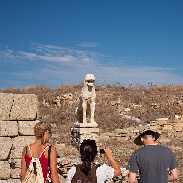 Mykonos, Greece  - September 9, 2010: a group tourists in front of one the Lions of Delos (guardians of the sacred island) during a visit to the archaeological site of Delos. Delos is a UNESCO World Heritage Site, it attracts many tourists and lovers of archeology.
