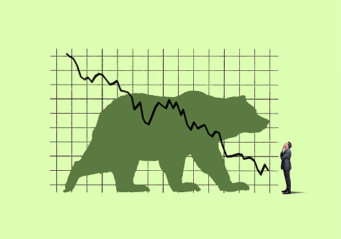 A businessman places his hand on his chin as he looks up at a large chart that indicates declining performance and has bear on it.