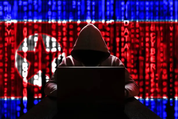 Cyber threat from North Korea. North Korean hacker at the computer, on a background of binary code, the colors of the flag of the DPRK. DDoS attack