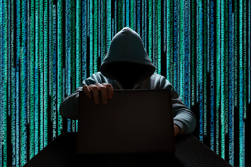Hacker cyber attack. Unknown hacker in the hood with a laptop on a background of binary code