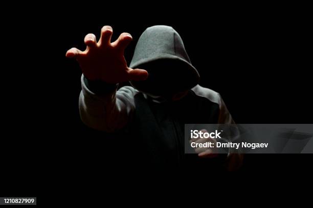 A Man In A Hood Reaches Out From The Darkness Robbery And Fraud Stock Photo - Download Image Now