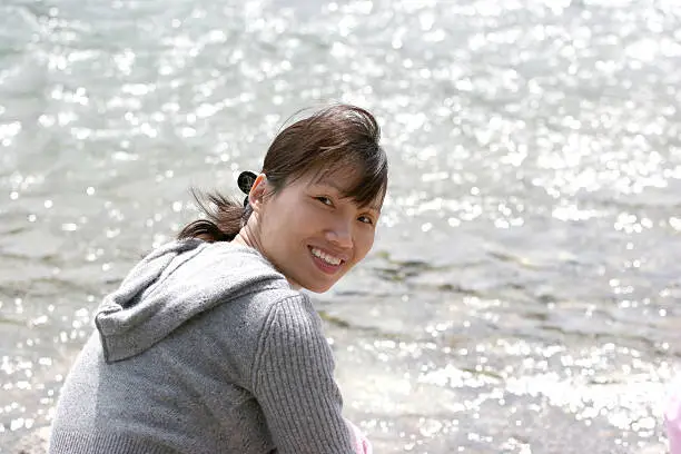 A pretty asian woman relaxes by the water's edge.