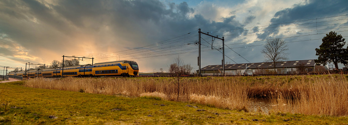 Panoramic view on Dutch passenger train against sunset sky