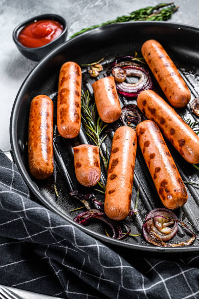 istock Fried sausages with garlic and herbs in a pan. Black background. Top view 1210842551