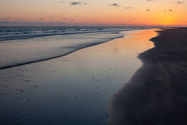 istock Ocean beach with orange glow after sundown reflecting in shallow waves on the sand 1210846835