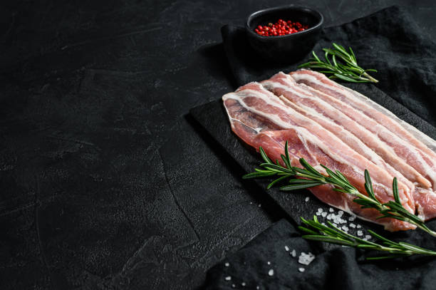 istock Raw bacon on a stone chopping Board. Pork meat. Black background. Top view. Space for text 1210853879