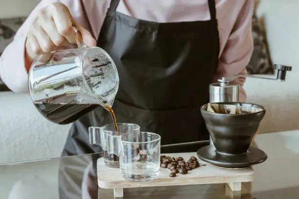 Photo of Cropped shot view of Barista pouring hot water on ground coffee with paper filter to make a drip coffee.