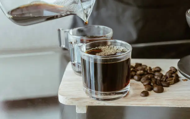 Photo of Cropped shot of Barista pouring a hot coffee after drip in a glass cup of coffee.