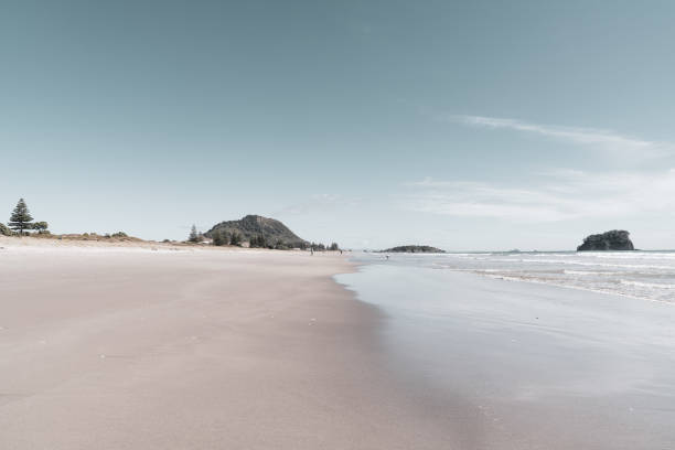 Ocean beach with Mount Maunganui at end, wide and flat sandy area in vintage effect.