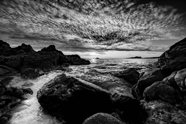 istock Sunrises over distant horizon along beach from rocky foreground 1210880171