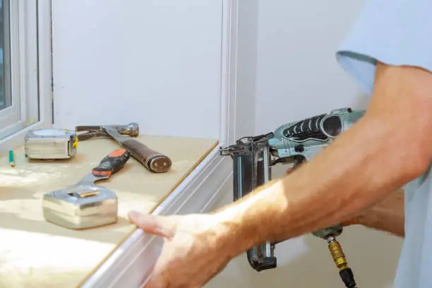 Carpenter close up using on air nail gun to moldings for window