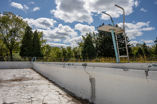Abandoned empty swimming pool in decay with white puffy clouds in the sky on a sunny day