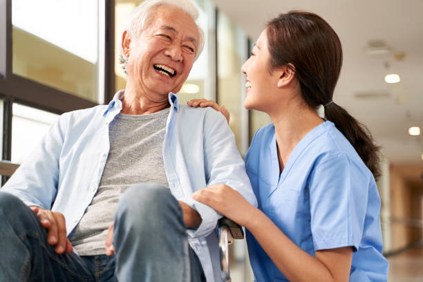 friendly asian caretaker talking to senior patient in nursing home young friendly asian female caregiver talking chatting to happy senior man in hallway of nursing home orthopedics photos stock pictures, royalty-free photos & images