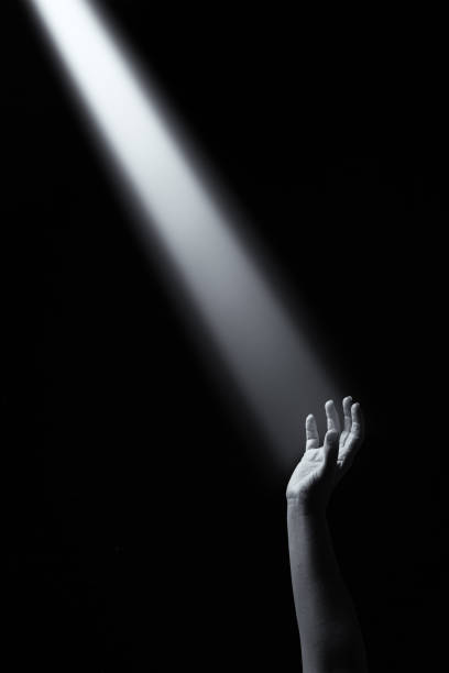 Artistic conceptual monochrome photo of a hand reaching into a beam of light stock photo