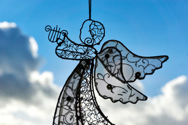 A christmas decoration angel with harp made of steel wire in front of a window. Blue sky with stormy clouds.