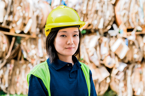 Confident female worker wearing hardhat. Portrait of woman is working at cardboard recycling center. She is at factory.