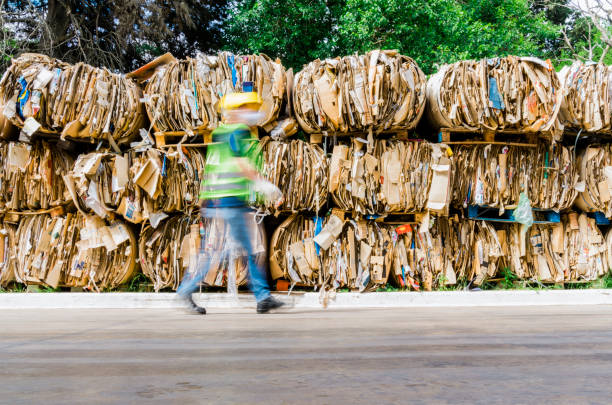 Blurred motion of man walking by cardboard stack. Male worker is working at recycling center. He is at waste management factory.