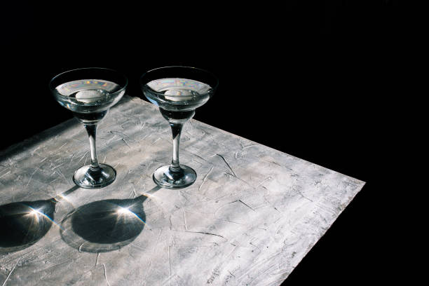 istock Glass goblets with a cocktail on a silver background. Glare and reflection from the sun. Minimal black background. 1210926130