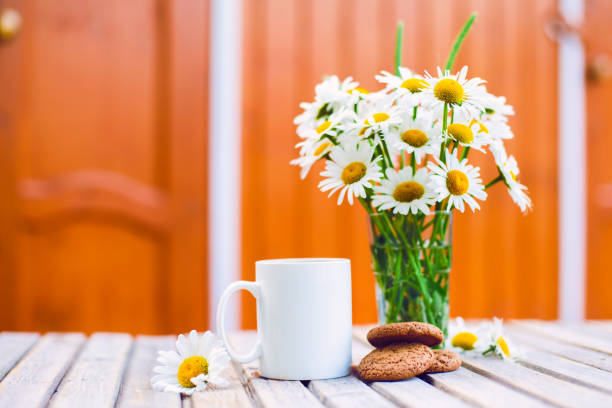 Cup of hot coffee,  biscuits and a bouquet of chamomiles on a rustic wooden background