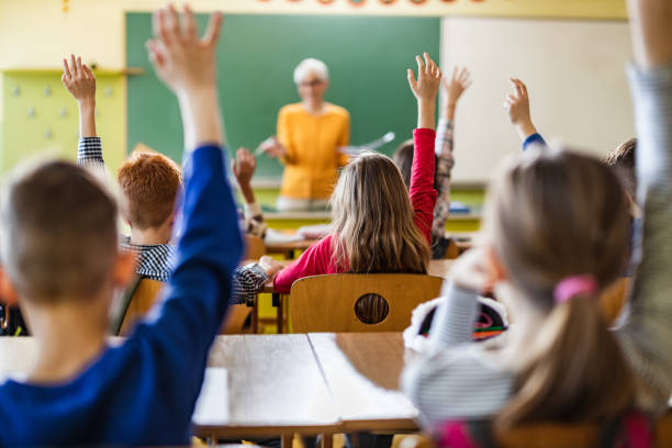 istock Back view of students raising their hands to answer the teacher's question on a class. 1210929233