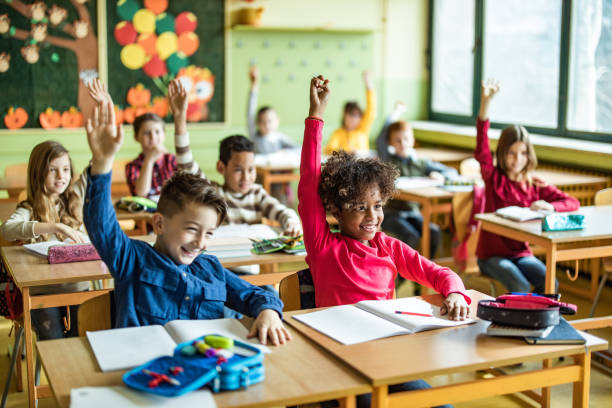 glückliche grundschüler heben ihre hände auf eine klasse in der schule. - kind im grundschulalter stock-fotos und bilder