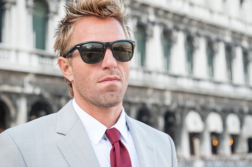 European businessman with tousled hair standing outdoors in front of classic Italian architecture in Venice, Italy