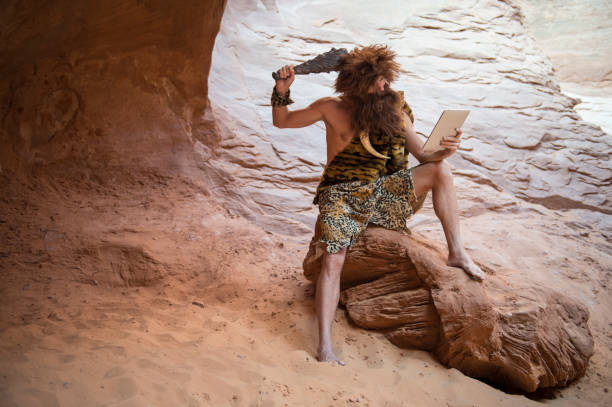 verwirrter caveman mit blick auf moderne tablets - steinzeit stock-fotos und bilder