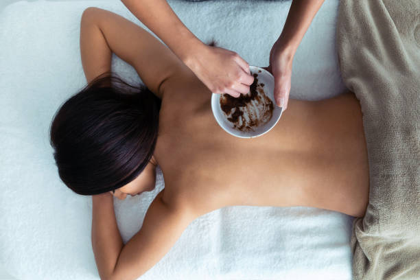 молодая женщина применения шоколадного крема с натуральными ингредиентами для лечения тела, чтобы красивая женщина на спа-центр. - massaging chocolate spa treatment body стоковые фото и изображения