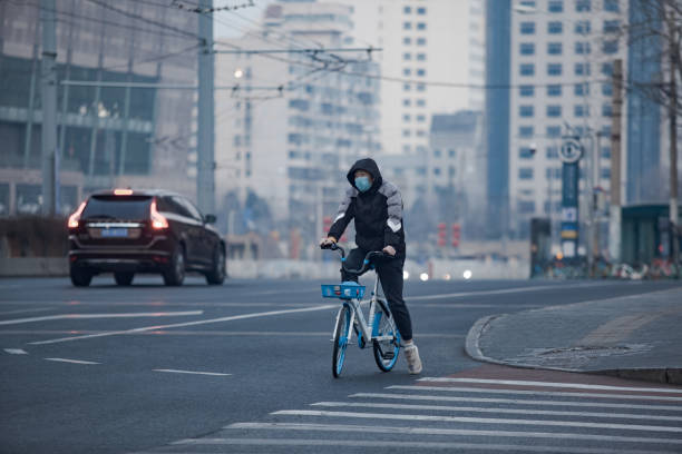 Coronavirus (covid-19) outbreak, chinese man riding a bike (bicycle) in the street wearing breathing mask due to danger of the virus, background buildings Due to the world concern about coronavirus (covid-19), and specially China, most of the citizens wear a mask in public spaces. Still, during the Chinese New Year in Beijing, people visited the monuments that were open, such as the Temple of Heaven, since the Great Wall and the Forbidden City were closed due to the danger of the virus. new year urban scene horizontal people stock pictures, royalty-free photos & images