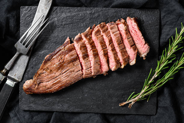 istock Grill Restaurant Beef Menu - Flank Steak on a black stone Board. Black background. Top view 1210939464