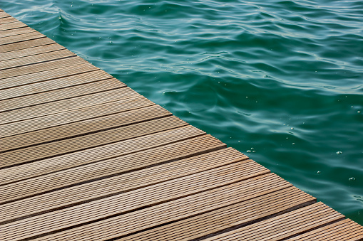 wooden deck floor background texture diagonal line and vivid blue and green water with small waves on a surface in big swimming pool, copy space pattern