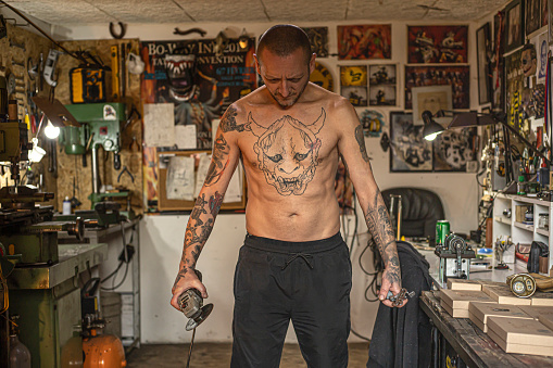 Man covered in tattoos holding a grinder in his workshop