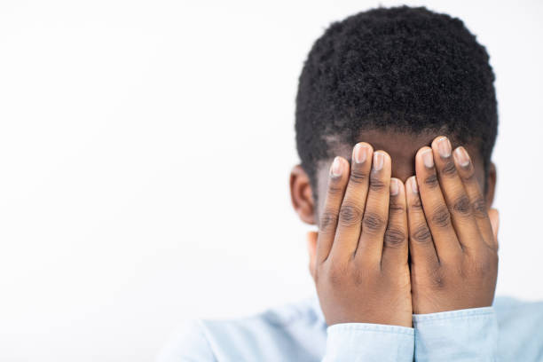 Unhappy Boy Covering Face With Hands Against White Background
