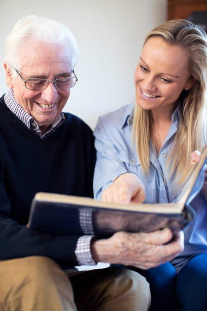 abuelo mirando álbum de fotos con nieta adulta - care community 80 plus years cheerful fotografías e imágenes de stock