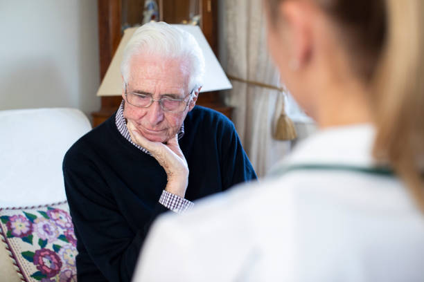 unglücklicher senior-mann wird von weiblicher krankenschwester besucht - senior adult depression dementia alzheimers disease stock-fotos und bilder