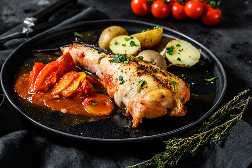 Cooking in tomatoes monkfish fish with baked potatoes. Fresh seafood. Black background. Top view.
