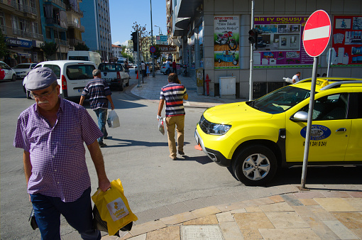 Denizli, Turkey - September, 2018: People crossing pedestrian on road intersection. Yellow taxi car and no entry traffic sign on one way road. Transportation city street scene.