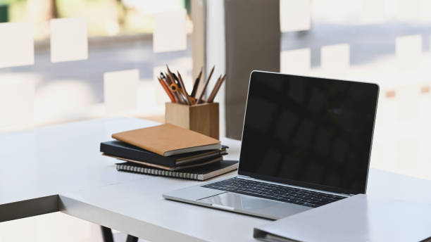 istock Computer laptop with blank black screen putting on the modern working table with wooden pencil holder, stack of books and document file. Orderly/Neat workplace concept. 1210948202