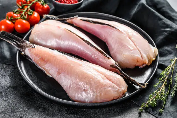 Photo of Separate raw fish monkfish. Black background. Top view