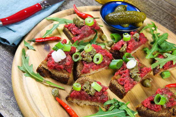 istock Hearty hefty german snack: isolated wood plate with roasted beef tatar garlic bread, spring onions, capers, pickled cucumbers (gherkins) and rucola salad leaves 1210951774