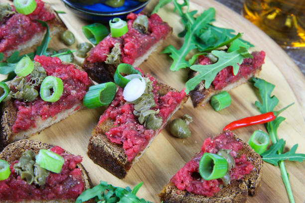 istock Hearty hefty german snack: isolated wood plate with roasted beef tatar garlic bread, spring onions, capers, pickled cucumbers (gherkins) and rucola salad leaves 1210951794