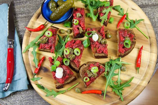 istock Hearty hefty german snack: isolated wood plate with roasted beef tatar garlic bread, spring onions, capers, pickled cucumbers (gherkins) and rucola salad leaves 1210951822
