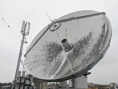 Huge retro satellite parabolic dish antenna on the roof for high speed internet link in front of overcast sky