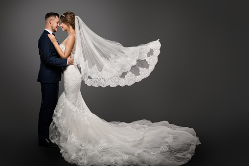 Wedding Couple, Beautiful Bride in White Dress and Long Veil, Elegant Groom Kissing Romantic Studio Portrait